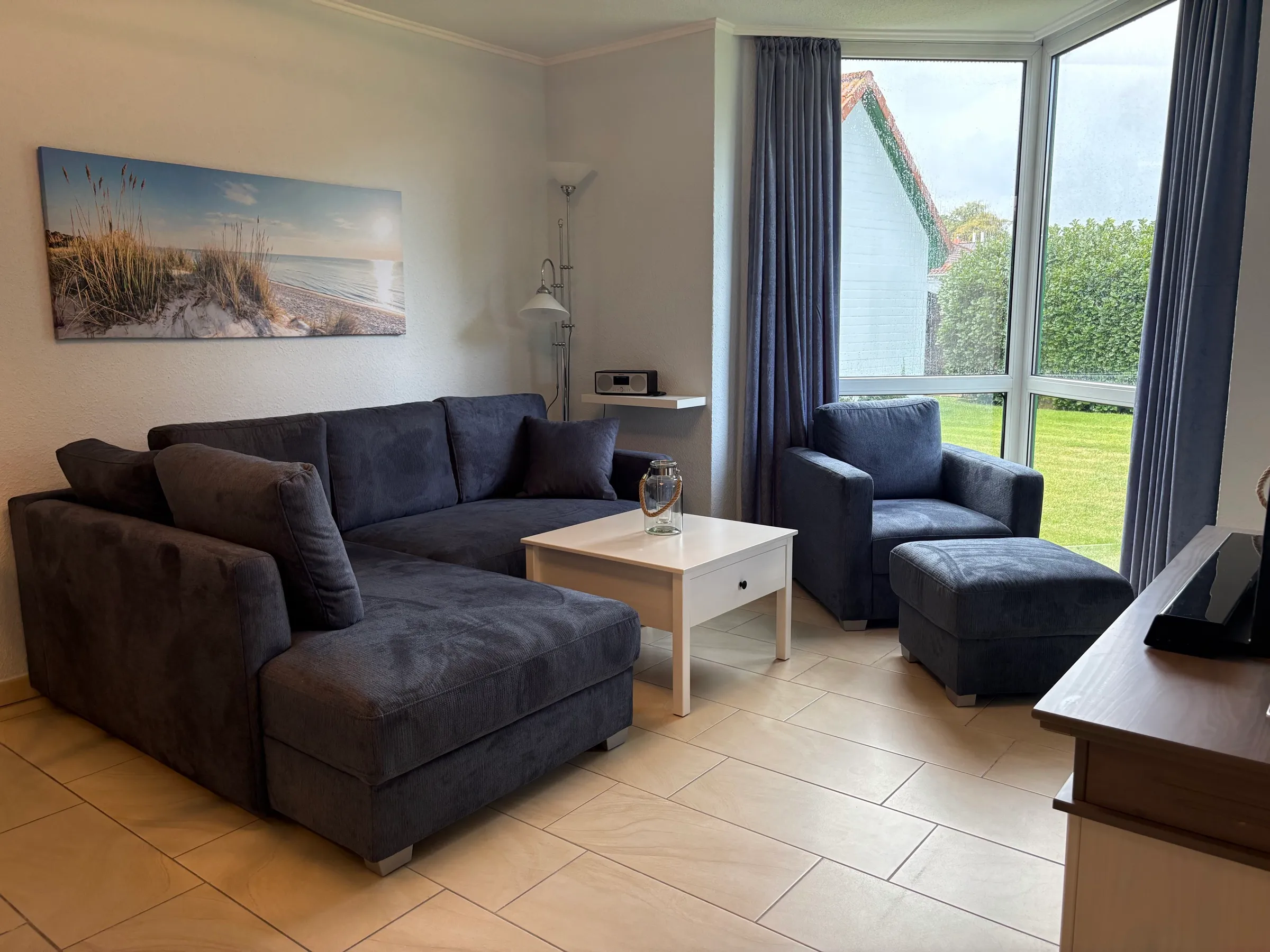 Wohnzimmer mit großer Sofaecke, Sessel und bodentiefem Eckfenster zum Garten