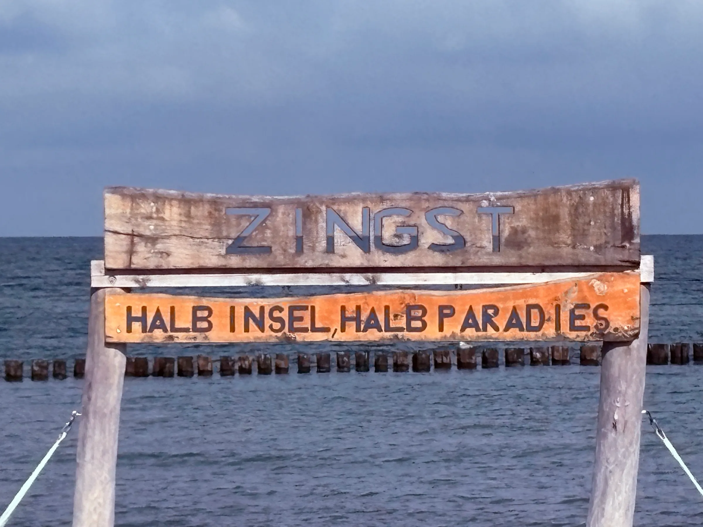 Holzschild „Zingst – halb Insel, halb Paradies“ im flachen Ostseewasser